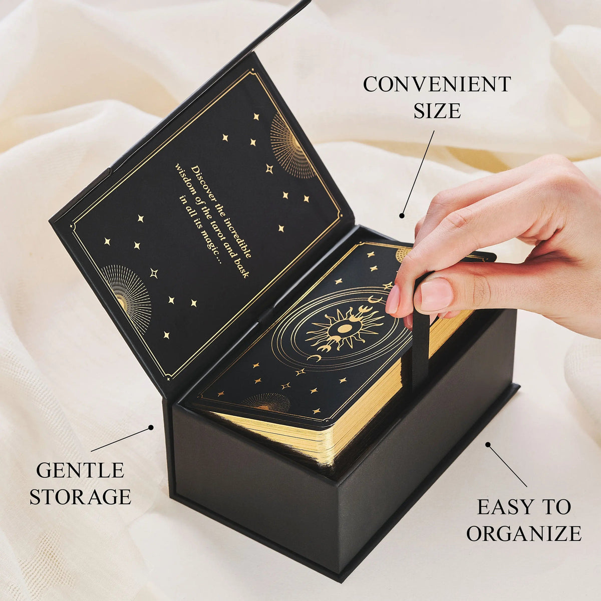 Black jewelry box with gold designs, open to reveal cards, on a white fabric background.